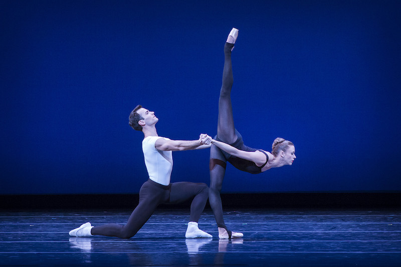 The male dancer is on one knee as he clasps his hands on his partner's. She extends her leg in an arabesque penchee 